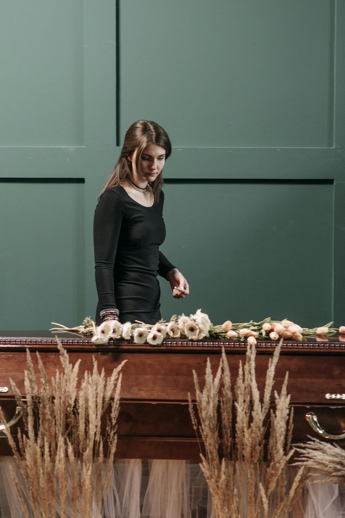 A young woman arranges flowers on a coffin, reflecting solemn emotions indoors.